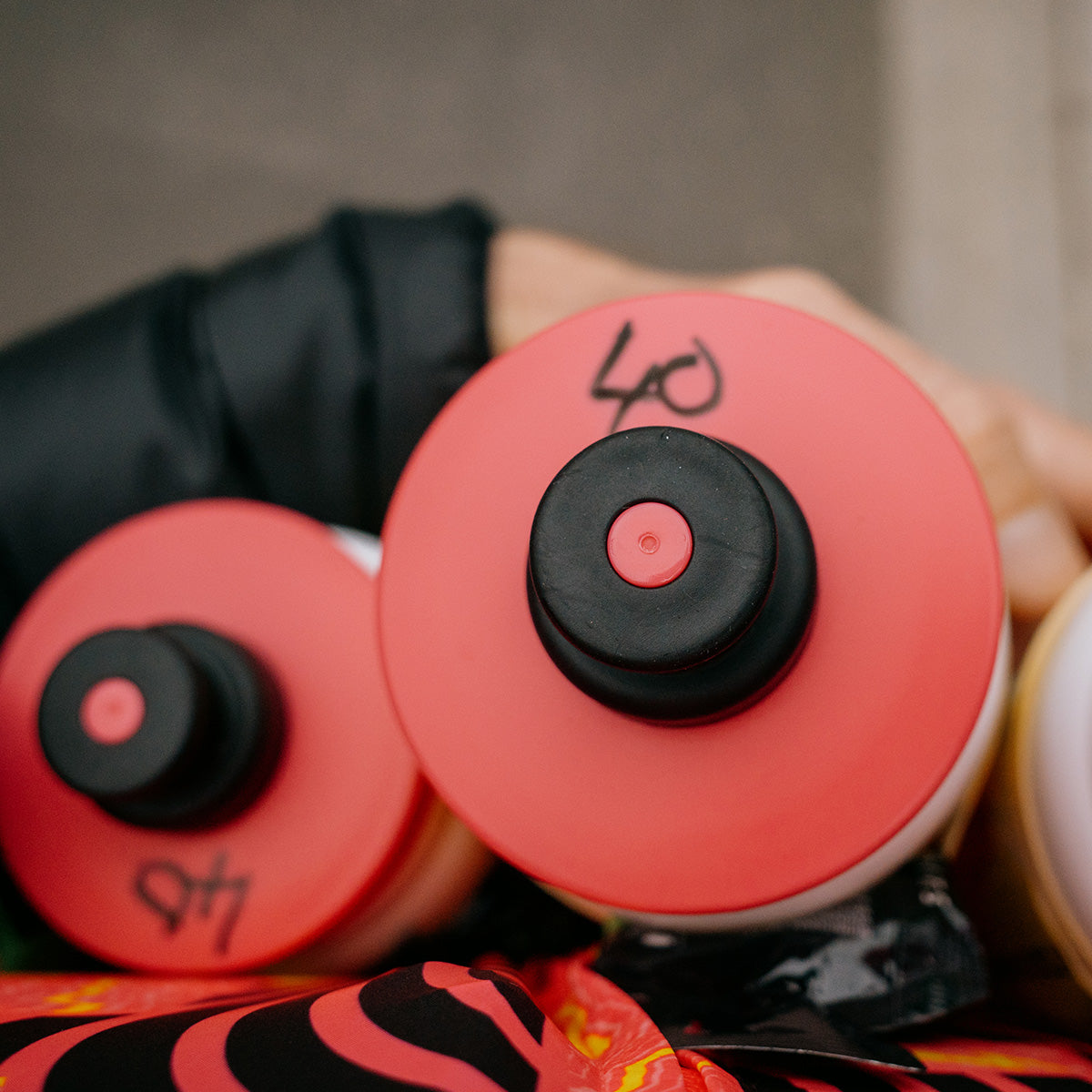 Close-up of red and black caps on bottles of Amacx Turbo Drink Watermelon held by a person wearing black clothing