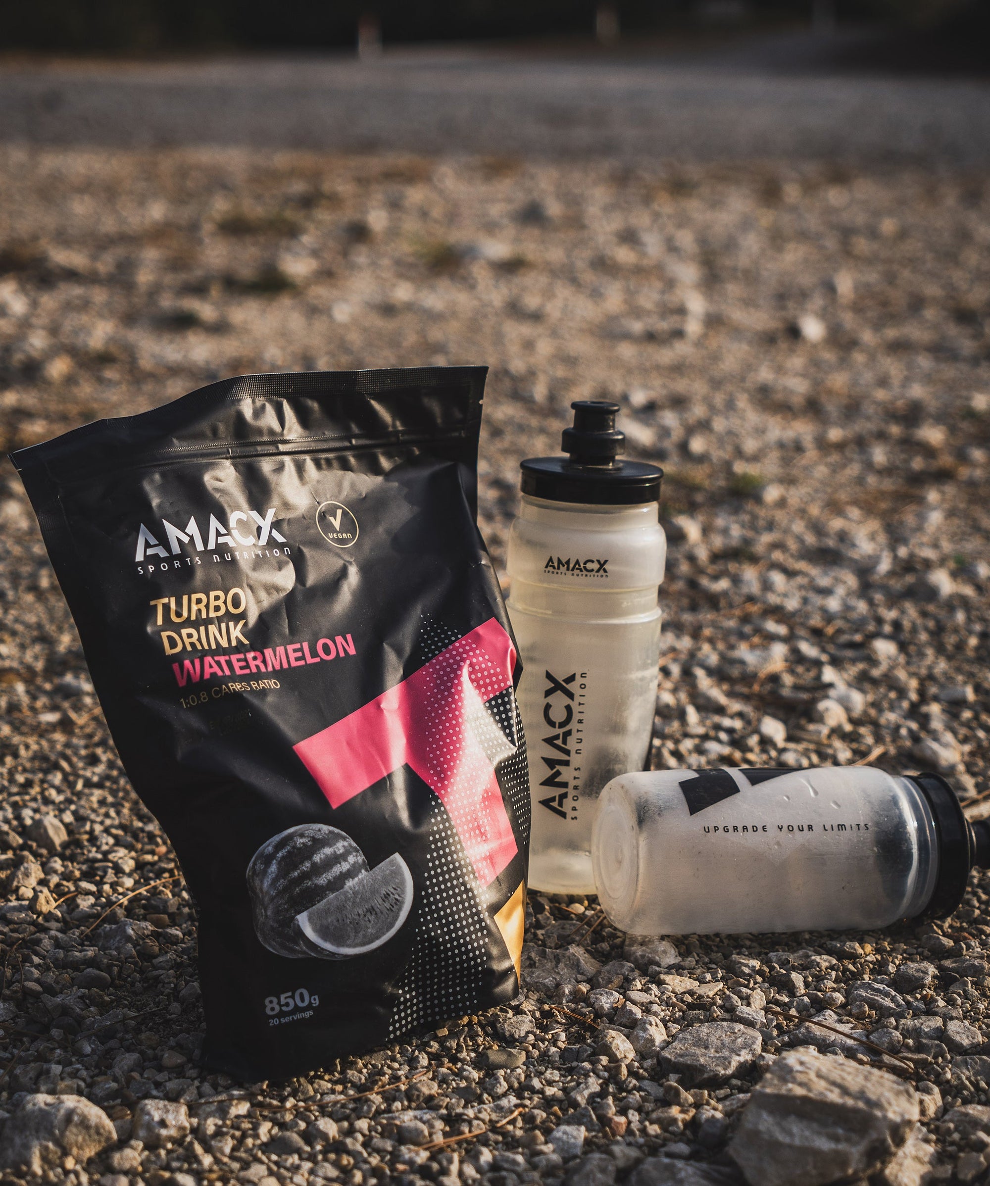 Amacx Turbo Drink Watermelon powder pouch with two branded shakers on rocky ground outdoors