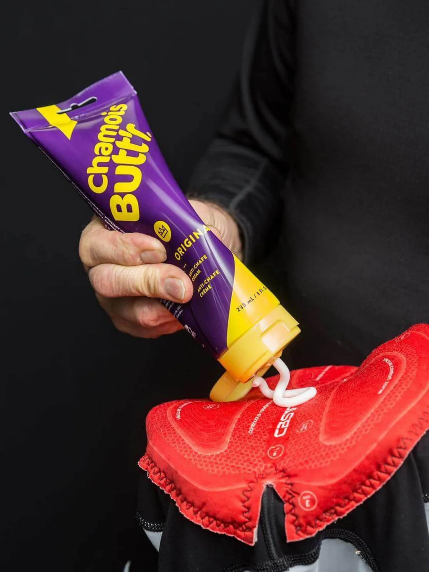Person applying Chamois Butt'r Chamois Cream - Original onto red cycling shorts padding for comfort and protection