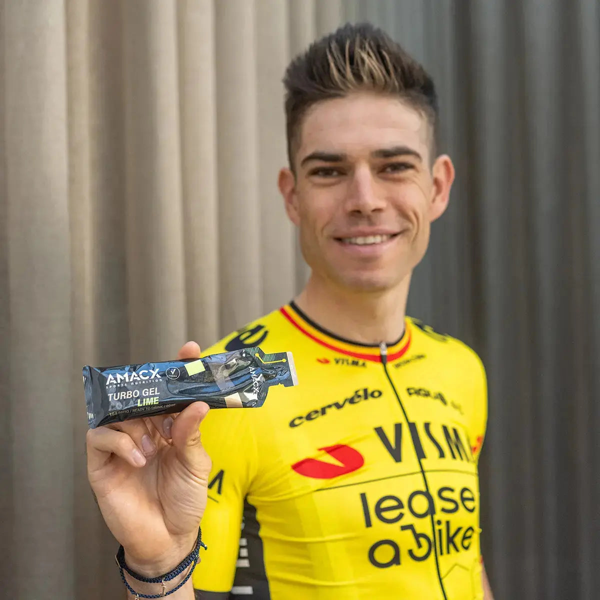 Athlete in yellow cycling jersey holding a single packet of Amacx Turbo Gel Cola Lime energy gel.