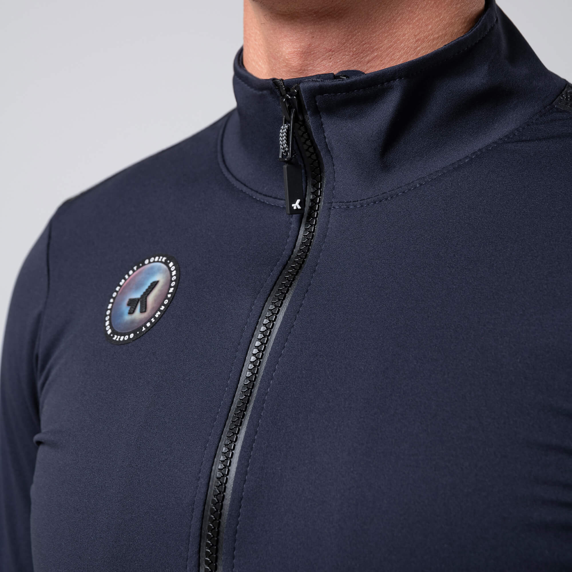 Close-up of a person wearing GOBIK Armour 2.0 Thermal Jacket - Unisex in dark color with front zipper and logo badge visible