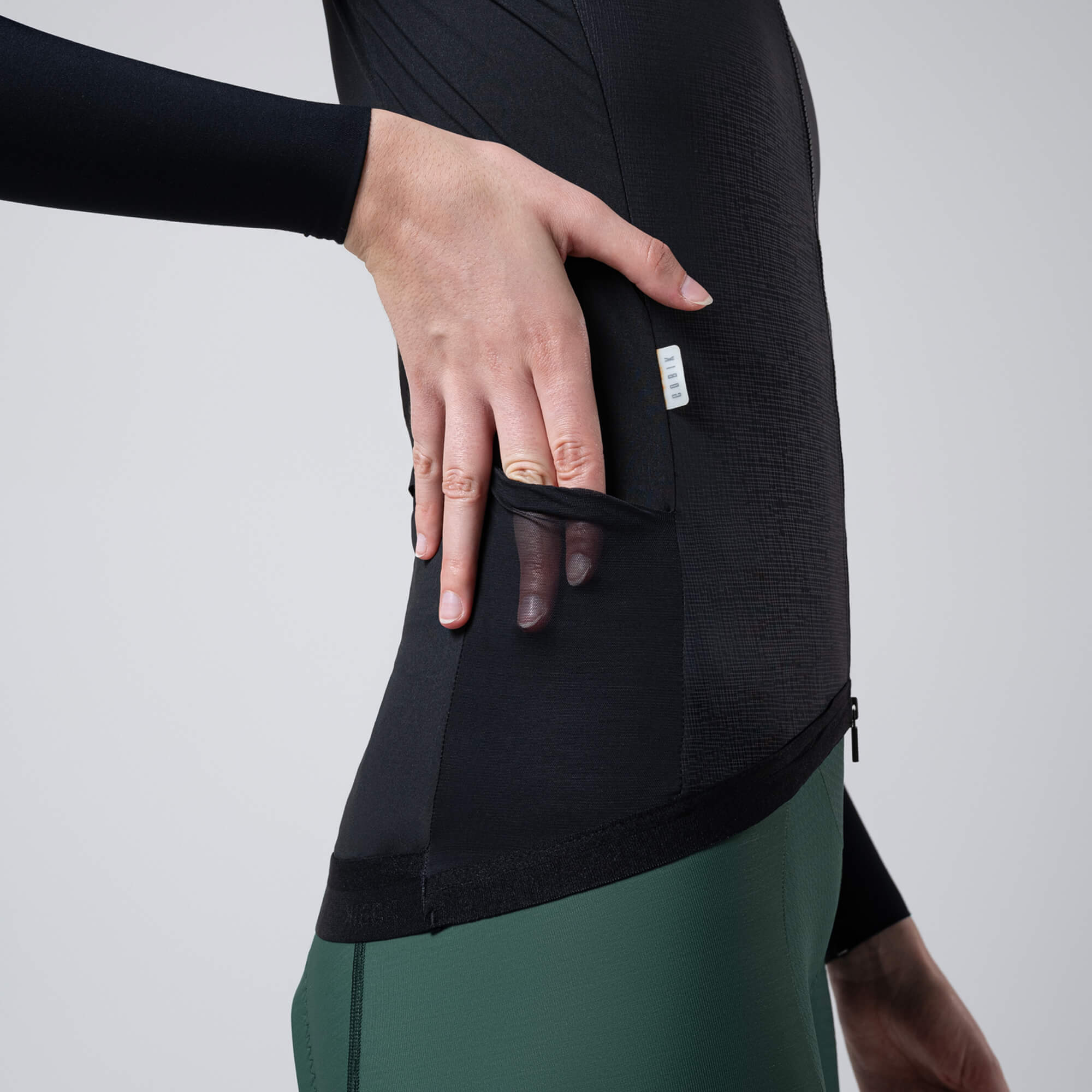 Close-up of hand opening side zip pocket on black GOBIK Vector 2.0 Vest - Women's showing fabric texture and fit details