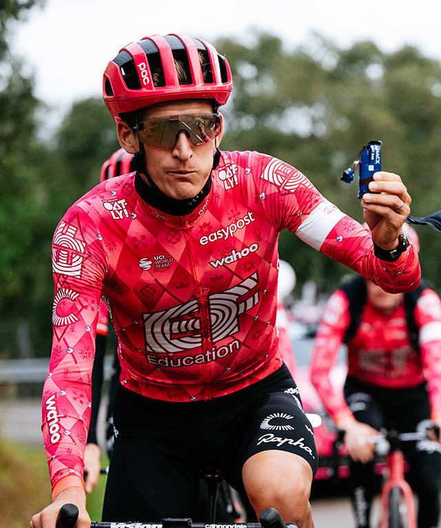 Athlete in red cycling gear holding Amacx Fast Bar Chocolate while riding a bike outdoors