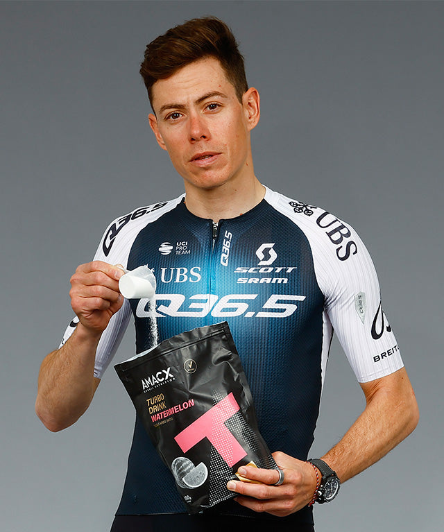 Athlete holding a black pouch of Amacx Turbo Drink Watermelon while scooping powder with a white measuring spoon