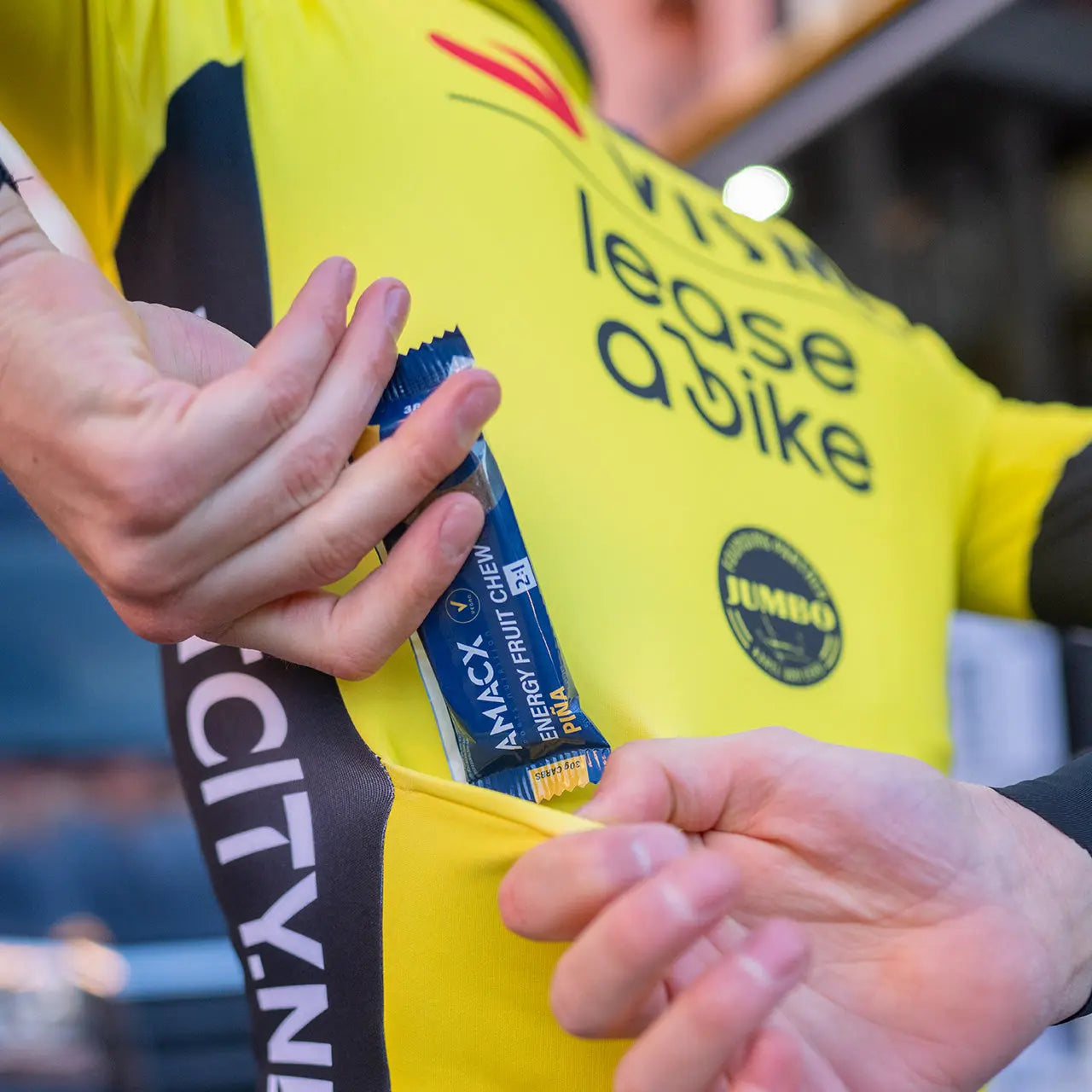 Person placing Amacx Energy Fruit Chew Piña pack into yellow cycling jersey pocket outdoors