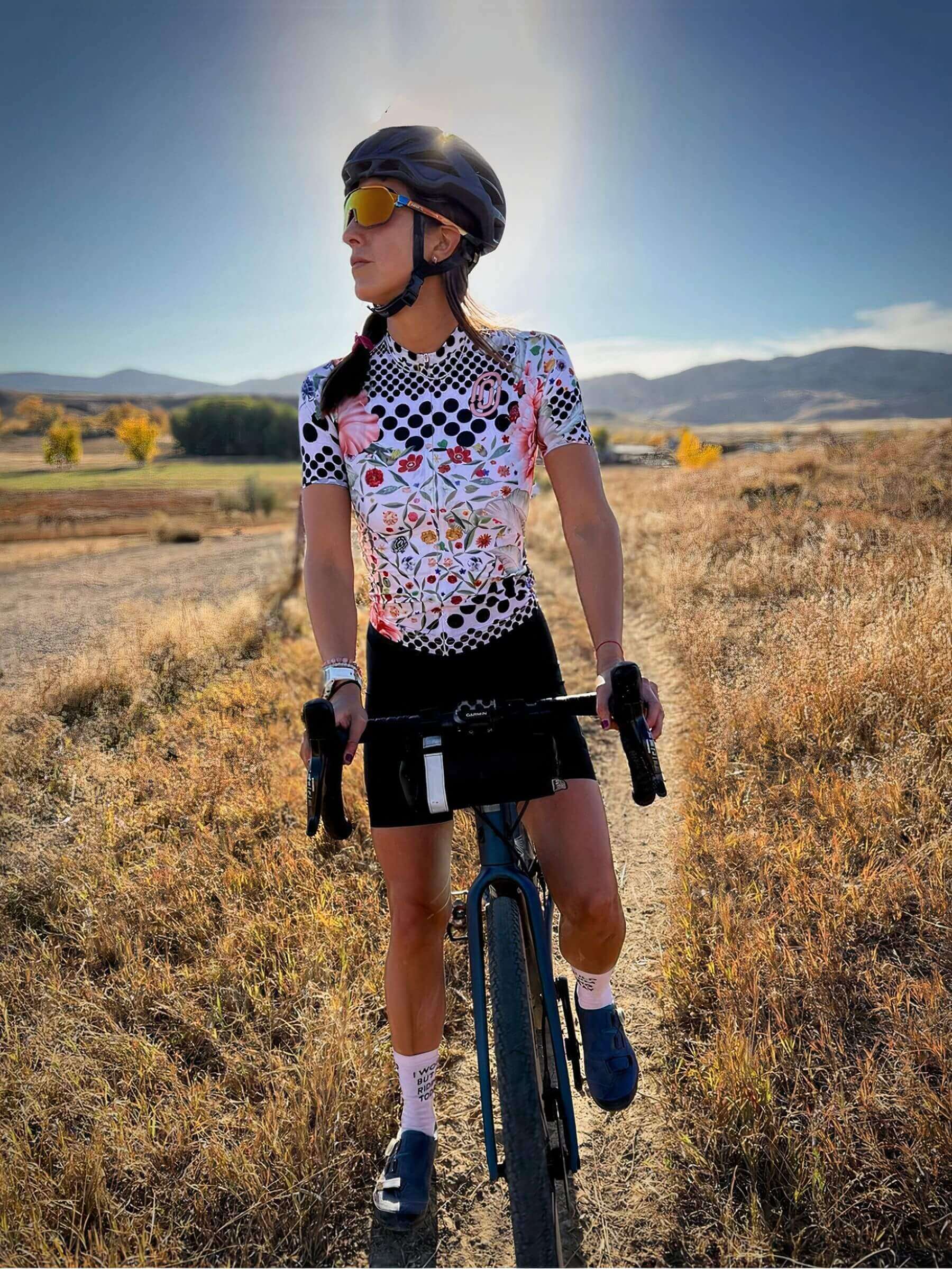 Woman wearing Ostroy Omloop White Jersey - Women's standing with bike in scenic outdoor field under clear sky