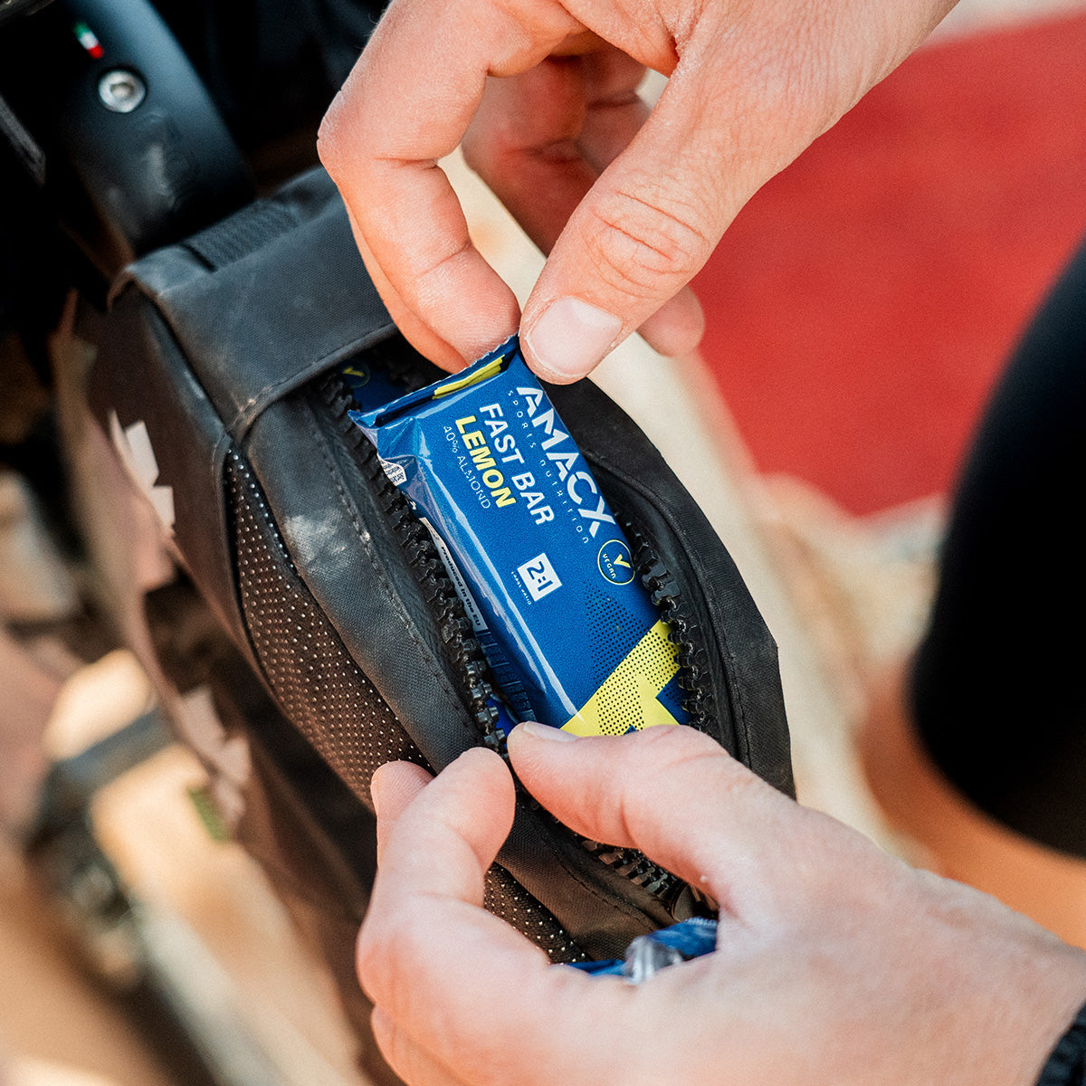 Hands placing an Amacx Fast Bar Lemon energy bar into a small bike storage pouch during a ride outdoors