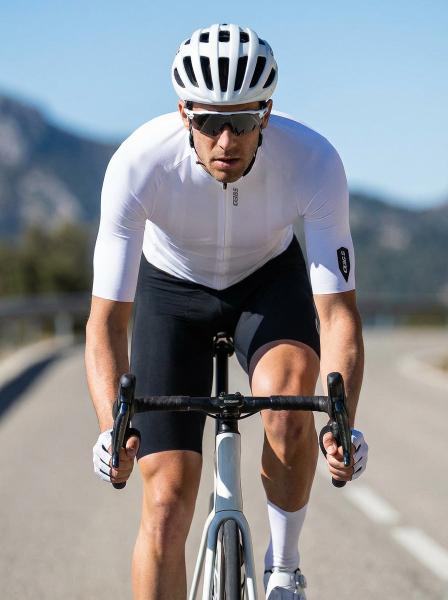 Cyclist wearing Q36.5 Gregrarius Pro Jersey - Men's - Cloud Dancer riding on a sunny road with mountains in background