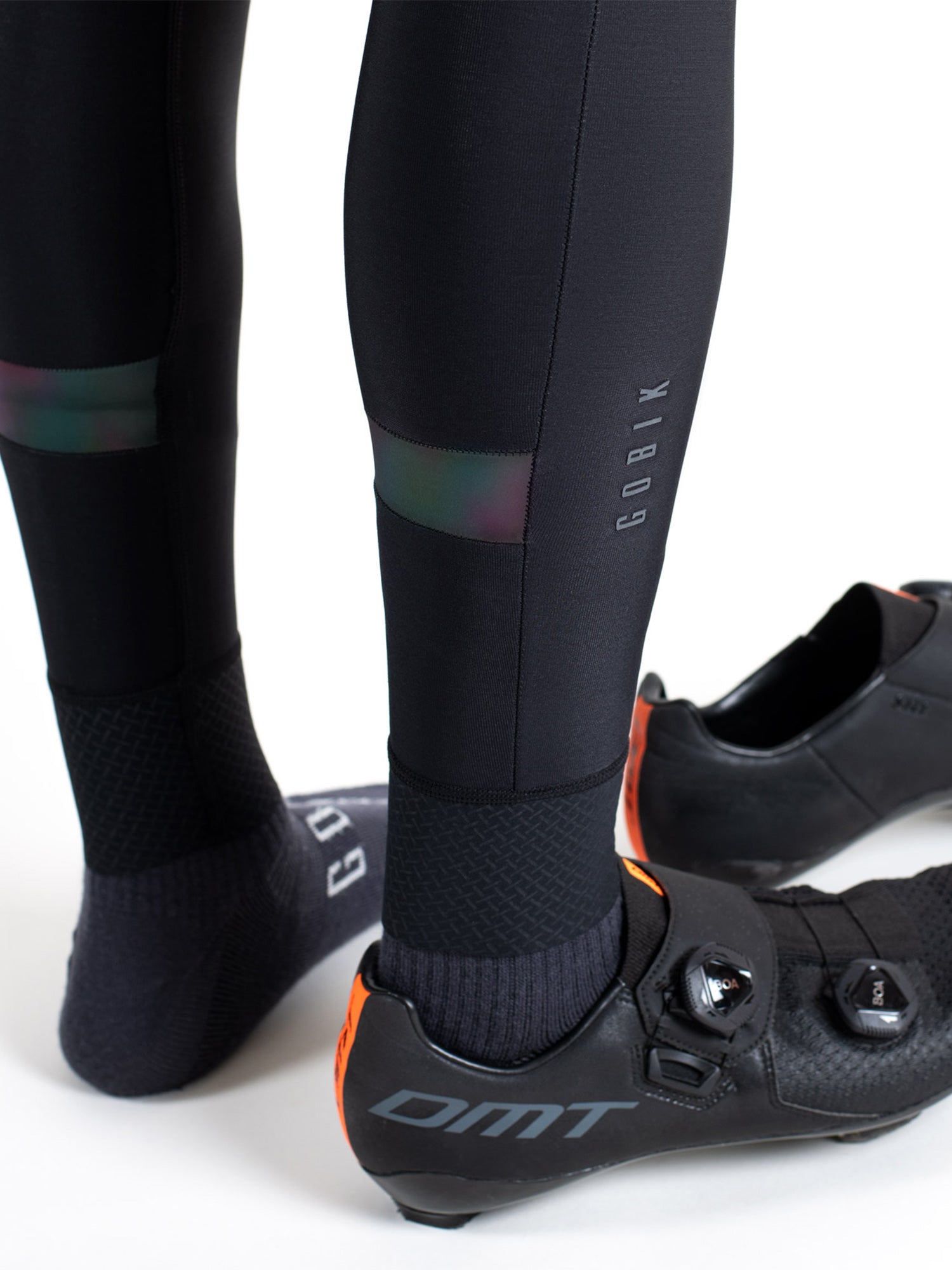Close-up of unisex GOBIK Kaba 2.0 Pitch thermal leg warmers on cyclist wearing black DMT shoes.