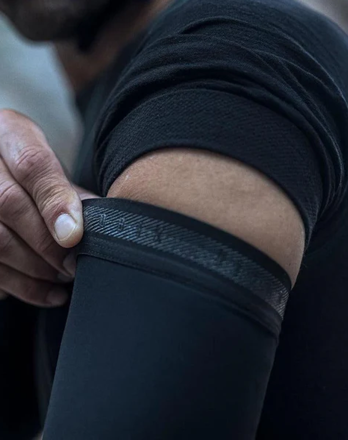 Close-up of a person adjusting GOBIK Haru 2.0 Lightweight Thermal Arm Warmers - Unisex with textured grip band in black